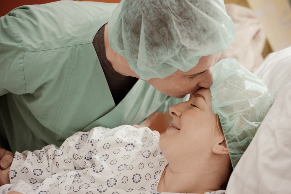 Ein Vater küsst die Mutter im Operationssaal auf die Stirn