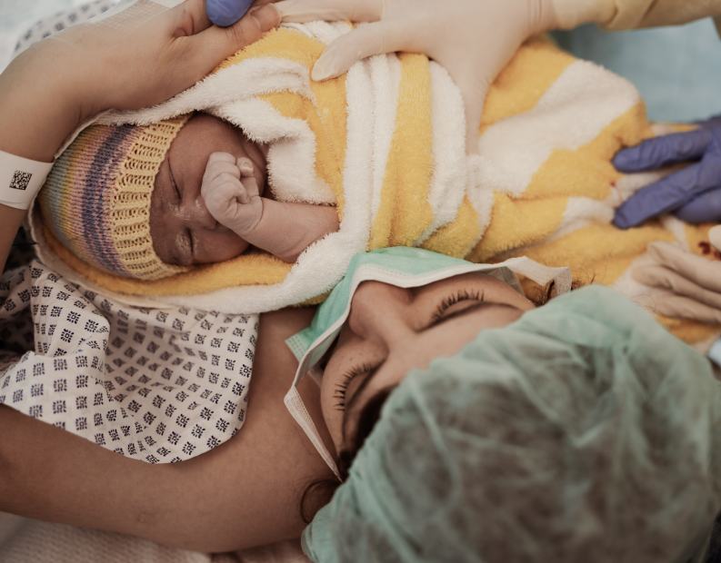 Ein Neugeborenes im Tuch dicht am Gesicht seiner Mutter