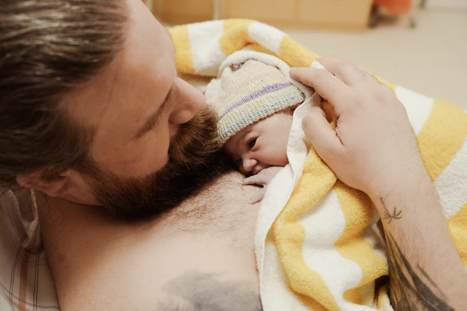 Ein Vater hält sein Neugeborenes auf der nackten Brust und küsst es