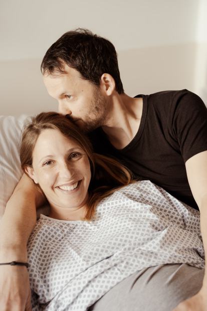 Ein Paar im Krankenzimmer, der Mann küsst die Frau auf den Kopf
