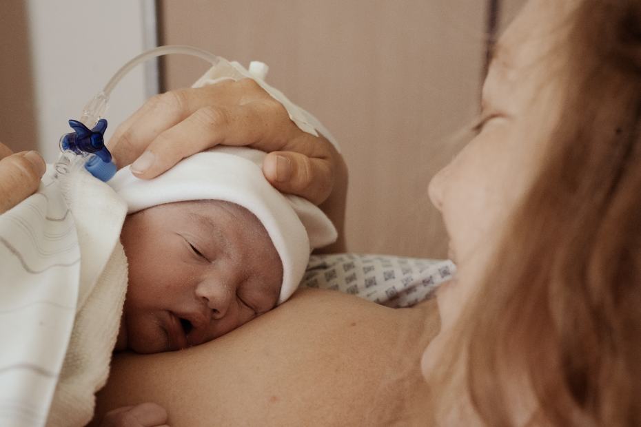 Ein Neugeborenes mit weißer Mütze schläft auf der Brust seiner Mutter