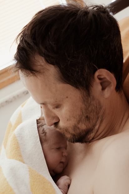Ein Vater küsst sein Neugeborenes, das er im Arm hält